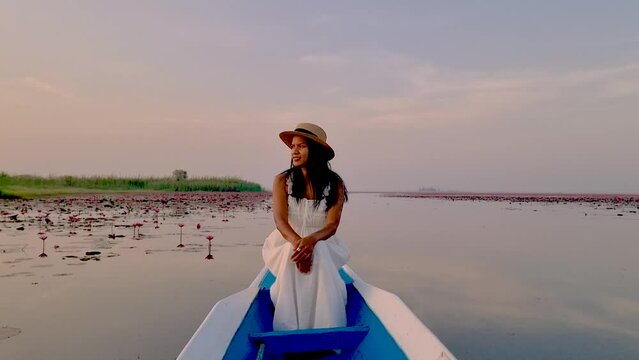 Asian women in a wooden boat during sunrise at the red lotus lake in Thailand , Sunrise at The sea of red lotus, Lake Nong Harn, Udon Thani, Thailand