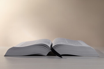 Naklejka premium Open Bible on white wooden table against beige background. Space for text