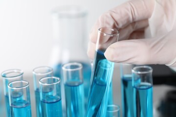 Scientist taking test tube with light blue liquid in laboratory, closeup