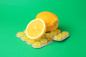 Blisters with cough drops and fresh lemons on green background