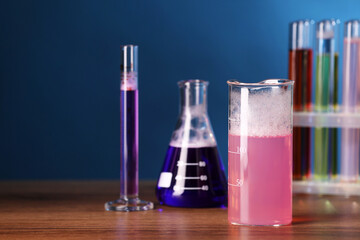 Laboratory glassware with colorful liquids on wooden table, space for text. Chemical reaction