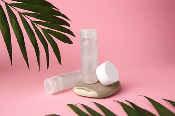 Cosmetic products, stone and palm leaves on pink background