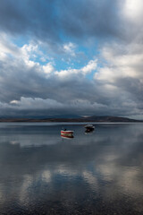 view of boat on still tranquil sea with reflection of clouds and sky on water