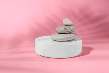 Fototapeta na wymiar Cosmetic product, stacked stones and shadow of tropical leaf on pink background