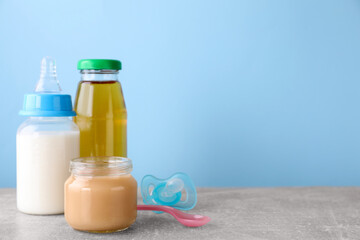 Jar with healthy baby food, milk, juice, pacifier and spoon on light grey table, space for text