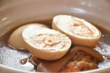 boiled half cut egg with fat pork leg in herb brown soup on bowl 