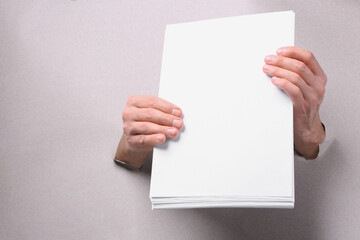 Man holding sheets of paper through holes in white paper, closeup. Mockup for design