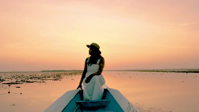 Sunrise at The sea of red lotus, Lake Nong Harn, Udon Thani, Thailand. An Asian women with a hat in a wooden boat during sunrise at the red lotus lake in Thailand 