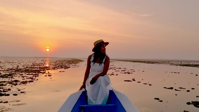Sunrise at The sea of red lotus, Lake Nong Harn, Udon Thani, Thailand. An Asian women with a hat in a wooden boat during sunrise at the red lotus lake in Thailand 