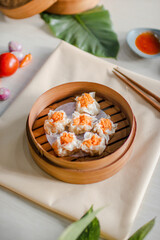 Top view traditional chinese steamed dumplings Dimsum in bamboo steamer on wooden table with chopsticks, sauce, chili and vegetable as decorations