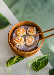 Top view of steamed prawn dimsum in bamboo steamer on wooden table with chopsticks, sauce and leaves as decoration
