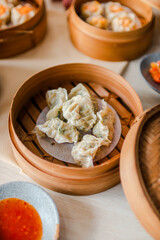 Close up of steamed dimsum in bamboo steamer on wooden table with chili and sauce as decoration