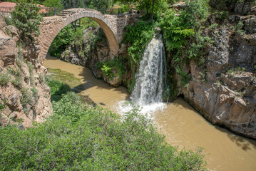 Fototapeta na wymiar View of Clandras bridge of Usak province with green nature and river and waterfall with blue cloudy sky
