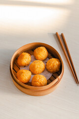 Deep fried chinese crispy Dim Sum in traditional bamboo bowl and chopsticks on light surface with copy space