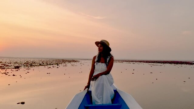 Sunrise at The sea of red lotus, Lake Nong Harn, Udon Thani, Thailand. An Asian women with a hat in a wooden boat during sunrise at the red lotus lake in Thailand 