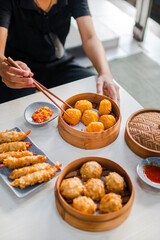 Close up female hand taking fried dimsum with chopsticks in traditional bamboo bowl on wooden table background