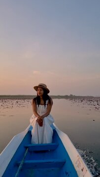 Sunrise at The sea of red lotus, Lake Nong Harn, Udon Thani, Thailand. An Asian woman in a wooden boat during sunrise at the red lotus lake in Thailand 