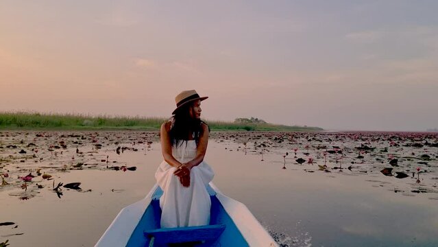 Sunrise at The sea of red lotus, Lake Nong Harn, Udon Thani, Thailand. An Asian woman in a wooden boat during sunrise at the red lotus lake in Thailand Isaan region