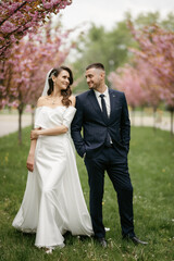 Naklejka premium newlyweds walk in the park among cherry blossoms