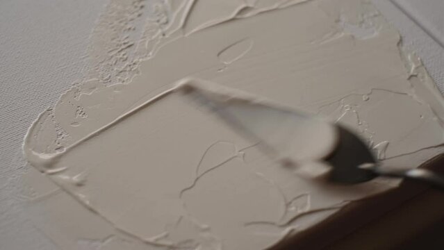 the artist draws a picture on the canvas with a palette knife close-up