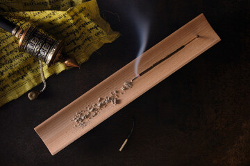 Overhead view of burning incense stick on wooden incense holder and tibetan hand prayer wheel on...