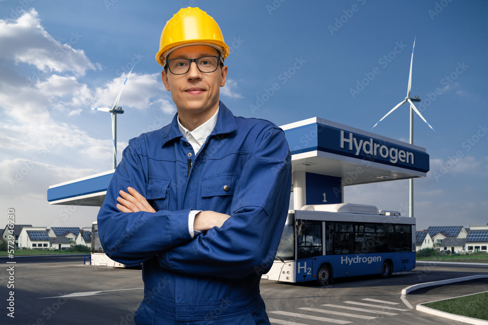 Poster engineer in a helmet and blue suit on a background of hydrogen filling station using renewable energ
