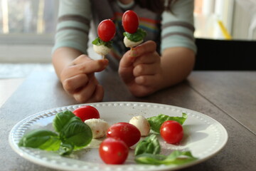 Child holding bocconcini cheese and tomato skewers