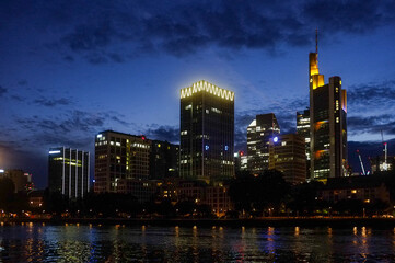 Stimmungsvoll beleuchtete Frankfurter Skyline bei Nacht mit blauem Himmel und dunklen Wolken