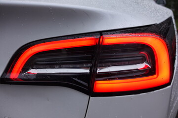 Sleek tail light of a silver fast car . Red lamp in parking position . The car is rainy and full of water drops . Car Detail View Close-Up Macro . Electric Tesla Car light from behind . Elektroauto .