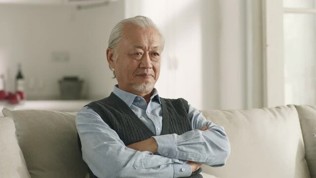 senior asian man sitting on couch at home looking sad or angry