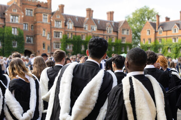 back view of Male and female fresh British Black African graduate students with gown and academic...