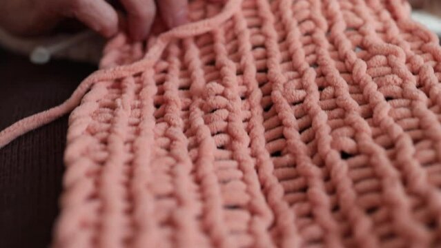 Close-up of a knitted item and women's hands with knitting needles