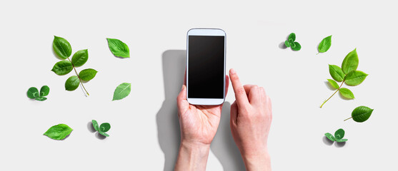 Person using a smartphone with green leaves - flat lay