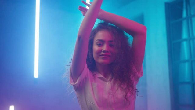 Video of a happy young woman dancing over neon light background at disco party