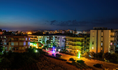 Night photography aerial shot of a city in alanya with residential apartment building houses, street with parked vehicles against dramatic blue sky