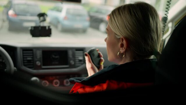 Young woman doctor sitting and talking in to walkie-talkie in ambulance car.