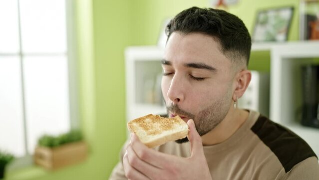 Young arab man eating toast sitting on table at home