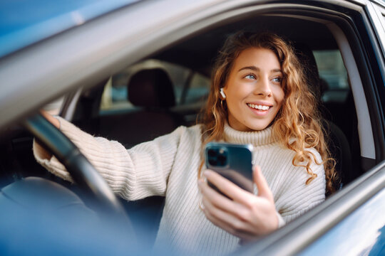 Young woman sitting in a car in the driver's seat looking into a smartphone, paying for parking and navigating in the city