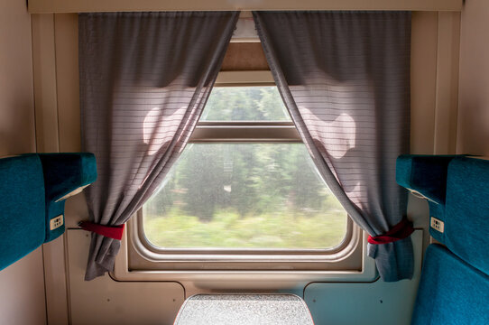A window and part of the interior of a compartment car inside a traveling train in summer