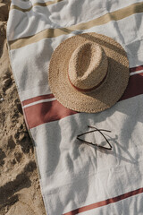 Flat lay female sunglasses, straw hat and beach towel on beach sand. Minimal aesthetic lifestyle fashion blog, magazine, social media. Sunbathe, relax, chill on summer travel vacations