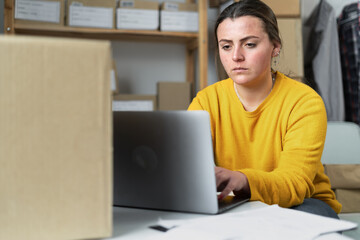Fototapeta premium Portrait of female online small business owner. Woman using a laptop with box. Success woman working online marketing with packaging box and delivery SME.