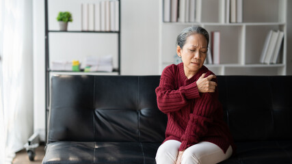 Senior Asian woman rubbing her shoulder, touch her shoulder to release the pain while sitting on...