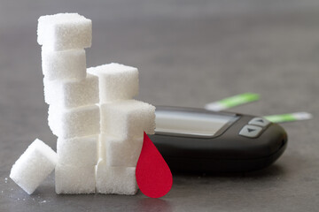 Stack of sugar cubes with red blood drop and glucometer, diabetes concept