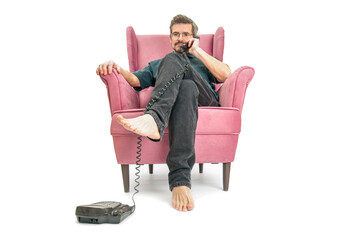 Adult man speaking on vintage phone in red comfortable armchair on white background