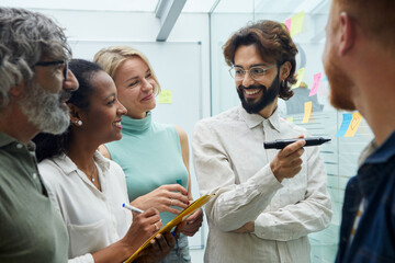 Meeting of creative colleagues in the office. Various workers from the team of business people standing around brainstorming, discussing and writing new ideas for the future of the company. 