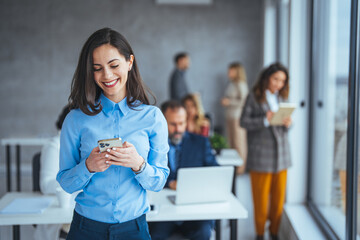 Young businesswoman in the office and texting on smartphone. Beautiful businesswoman using mobile phone in modern office. Businesswoman with smartphone sitting near the window and having fun 