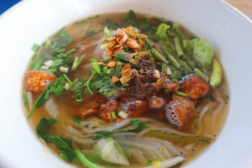 Delicious Khao Piak Sen (Lao Noodle Soup) with crispy pork and vegetables in white bowl