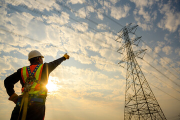 An electrician at a power station wearing a safety suit and hard hat prepares to inspect and...