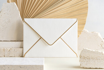 Blank envelope near beige stones against dry beige palm leaf close up, mockup