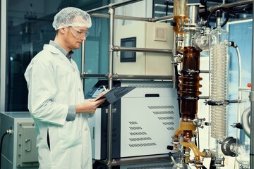 Apothecary scientist using a clipboard and pen to record information from a CBD oil extractor and a...